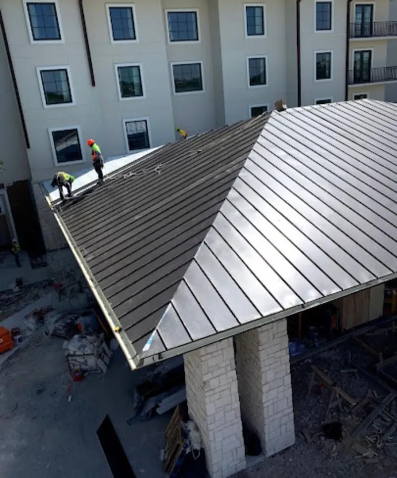 Crew installing standing seam metal roof panels on a commercial project in Prairie View